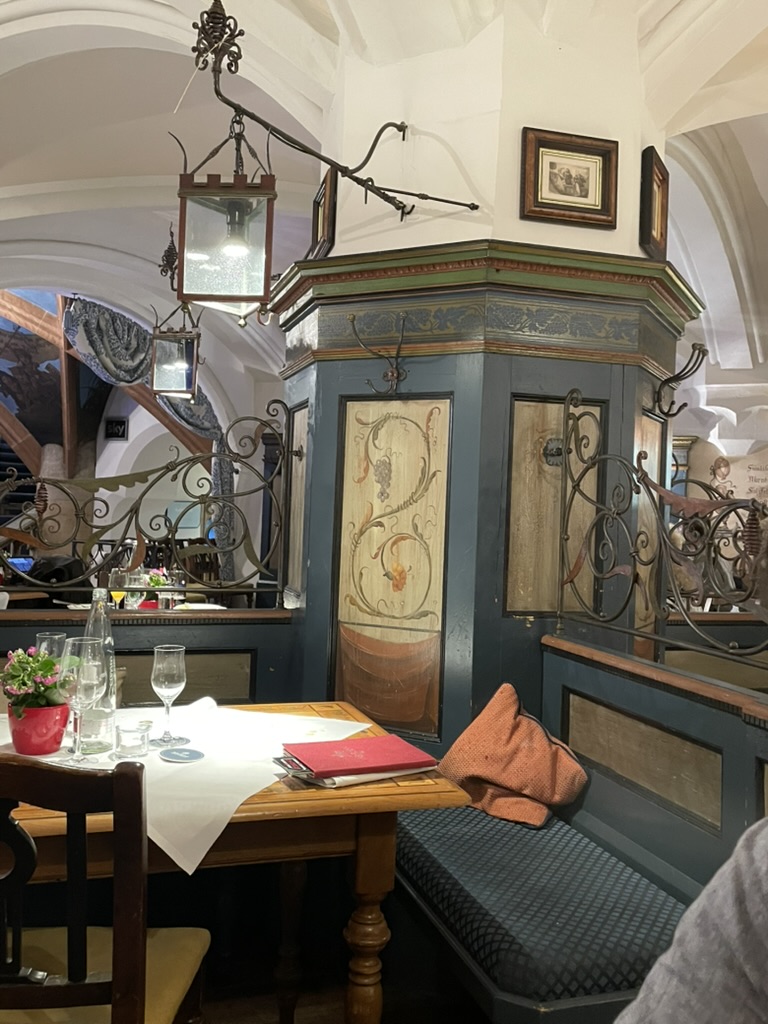 The cozy interior of the restaurant Ratskeller in Munich, featuring a wooden table set for dining, with decorative wrought iron elements and soft lighting.
