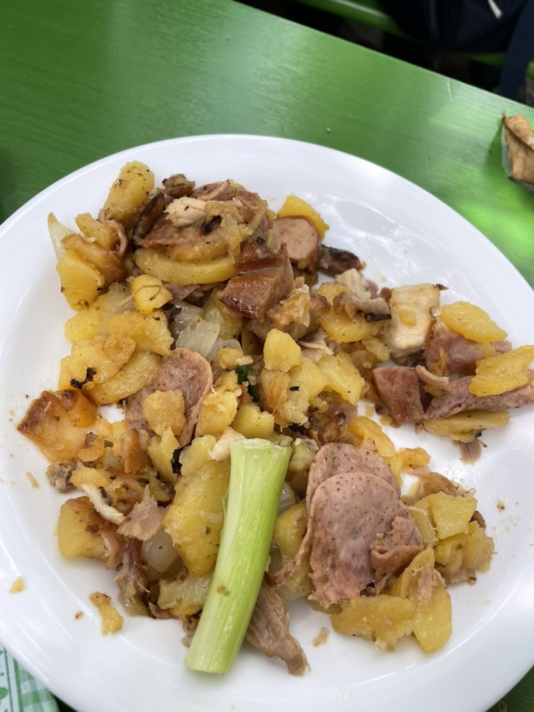 A plate of mixed potatoes, pork, and sausage, garnished with a green onion, on a green table.