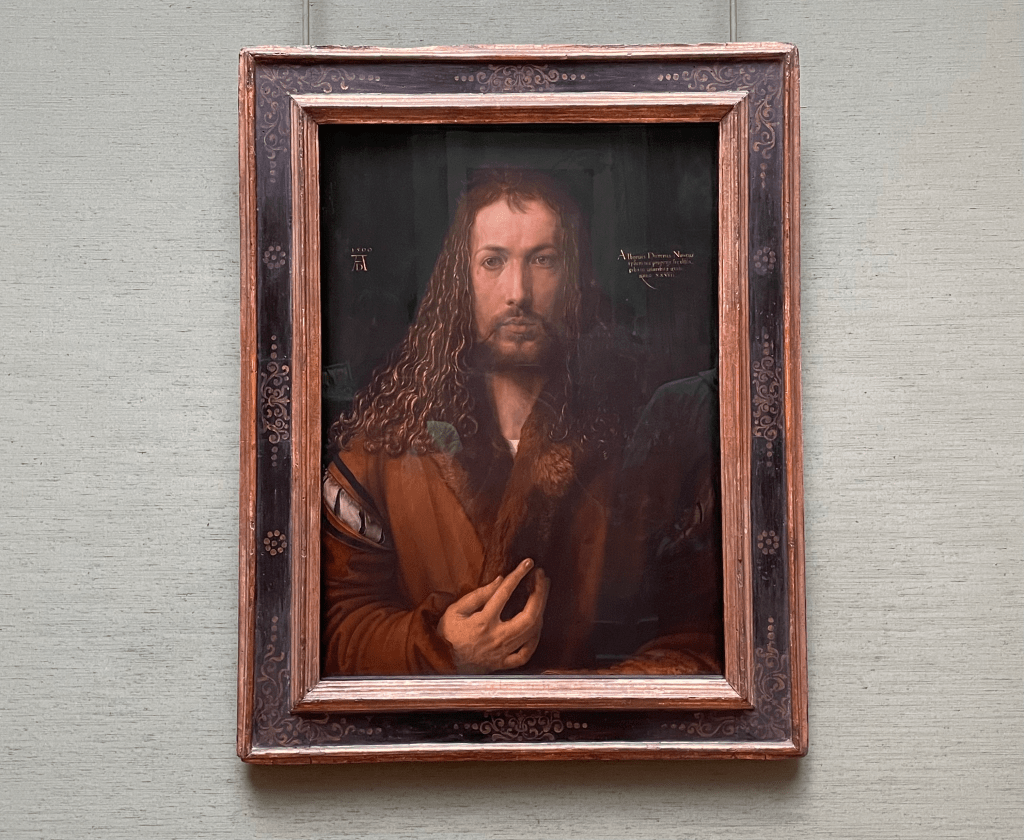 Self-portrait of Albrecht Dürer, featuring him in front of a dark background, wearing a fur coat, with long curly hair and an intriguing hand gesture.
